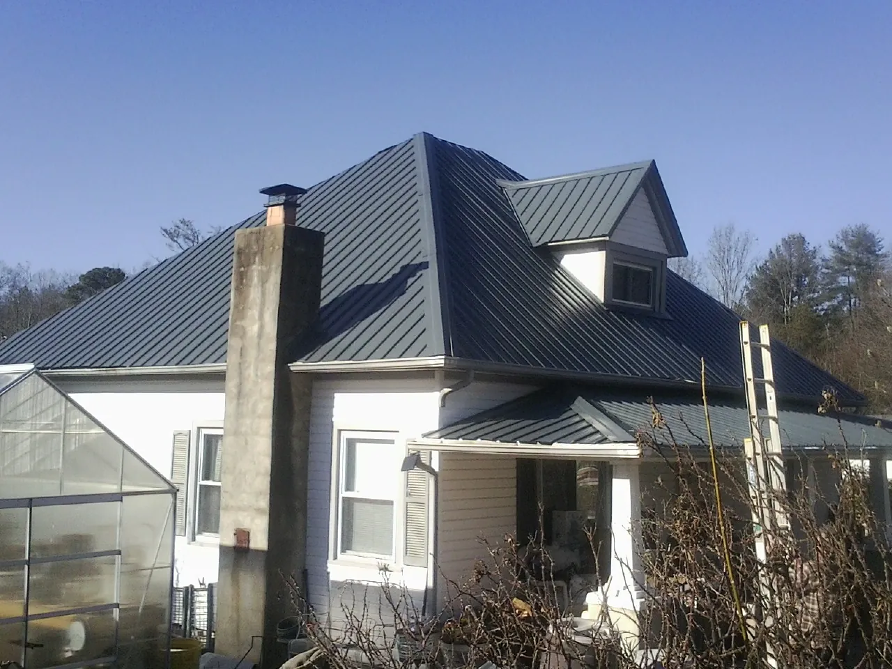 Dark blue standing seam metal roof on a white farmhouse with dormer — Slate & Tile Roof Repair by Roofing Brothers in New Ulm