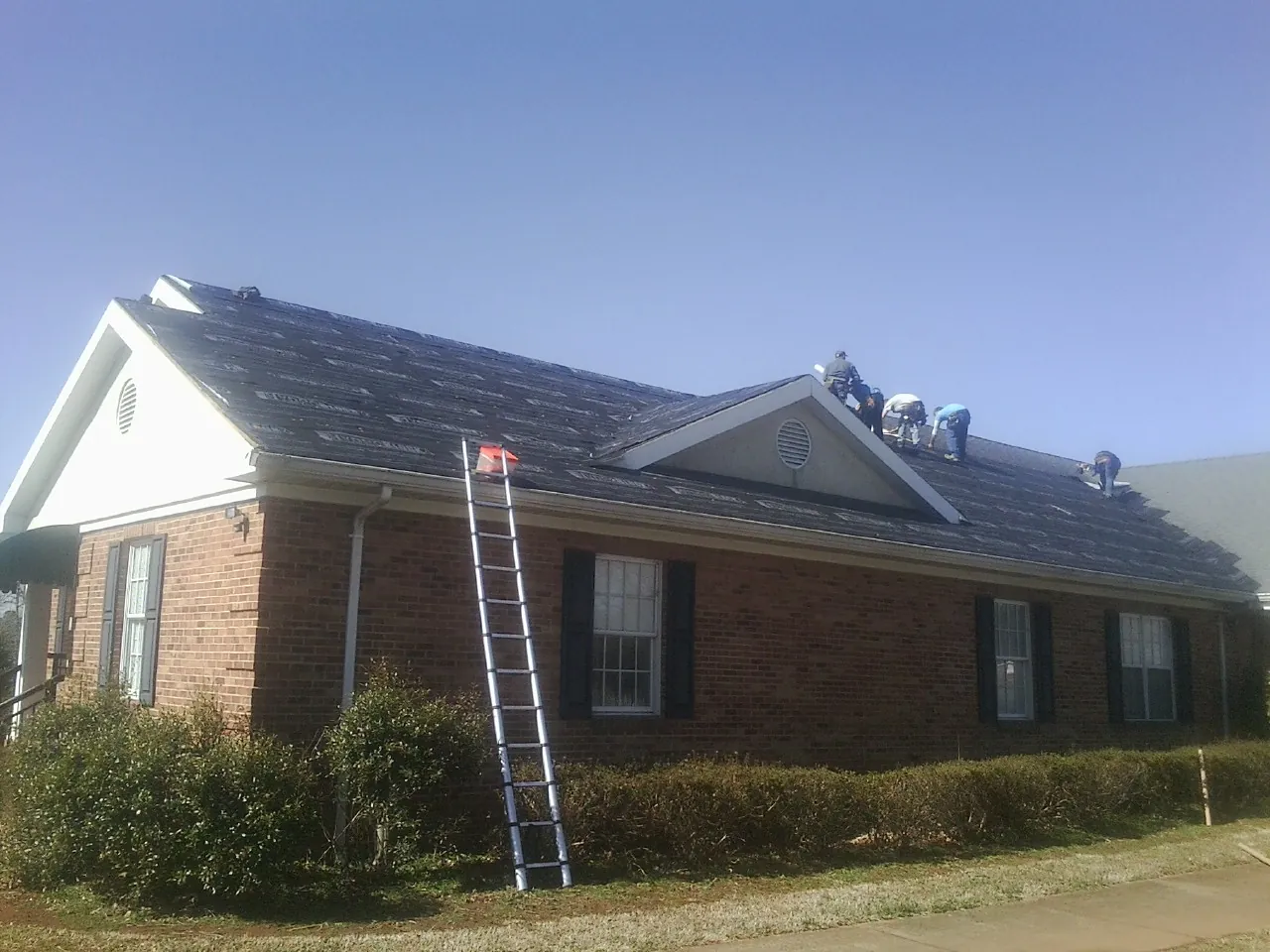 Crew tearing shingles off a brick ranch roof with a ladder set — Metal Roof Repair work by our crew in New Ulm