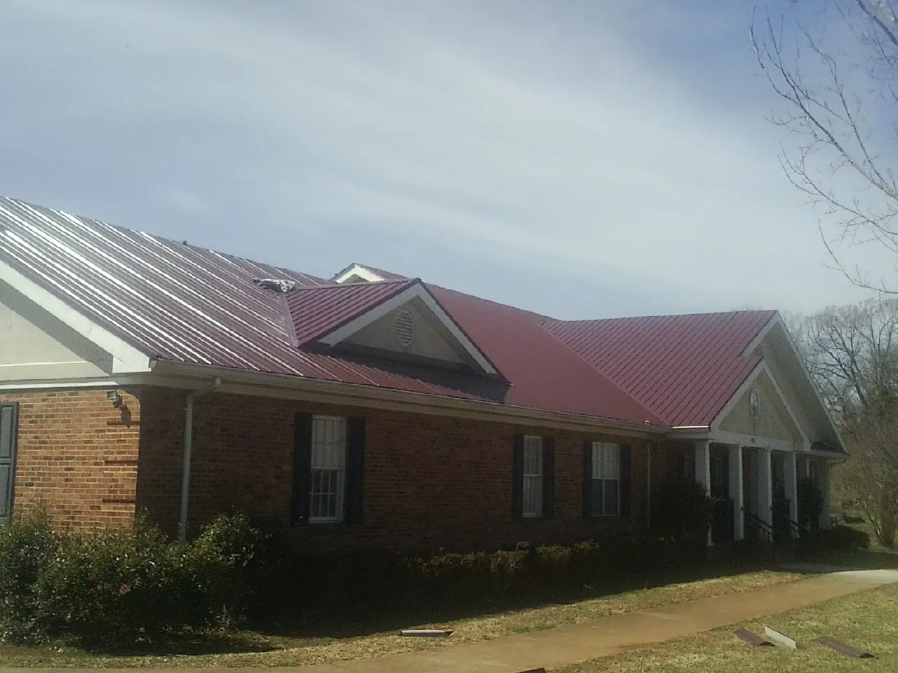 Red metal roof with gabled entries on a long brick building, from a Hail Damage Roof Repair job in New Ulm