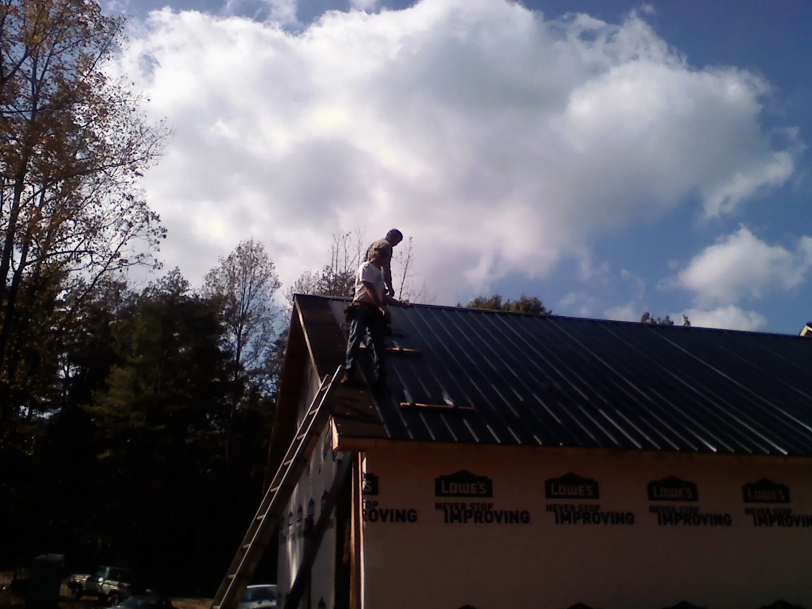 Roofer fastening dark metal panels high against a cloudy sky in New Ulm